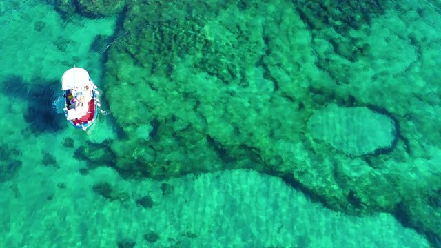 Aerial drone top view video of traditional fishing boat cruising in island of Mykonos deploying fishing net to catch fish, Cyclades, Greece