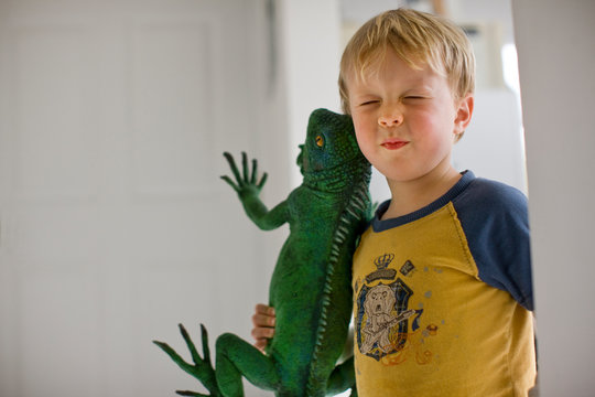 A young boy holding a large toy lizard.