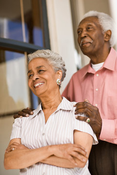 Senior African American couple smile whilst standing outisde a house. 