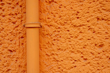 Orange verputzte Hauswand mit Rohrleitung