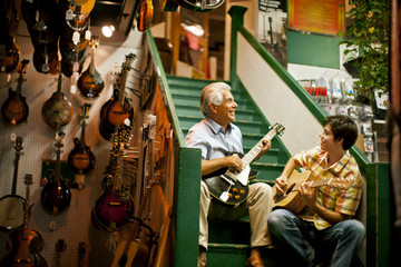 Smiling senior man playing guitar with his teenage grandson.