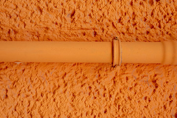 Orange verputzte Hauswand mit Rohrleitung