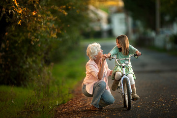 Little girl learning to ride her bicycle with the help of her grandmother.