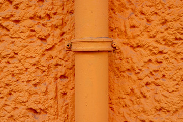 Orange verputzte Hauswand mit Rohrleitung