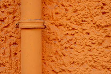 Orange verputzte Hauswand mit Rohrleitung