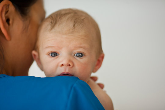 Portrait of a baby boy looking over a nurse's shoulder.