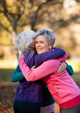 Three senior women hugging each other in a park.