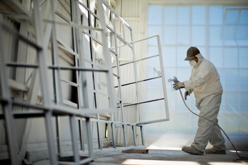 Mid adult man in protective clothing spray painting window frames inside a garage.
