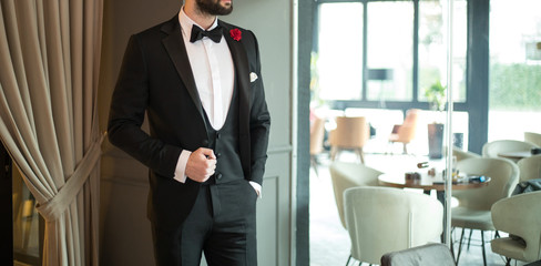 Man in expensive custom tailored suit, tuxedo standing and posing indoors