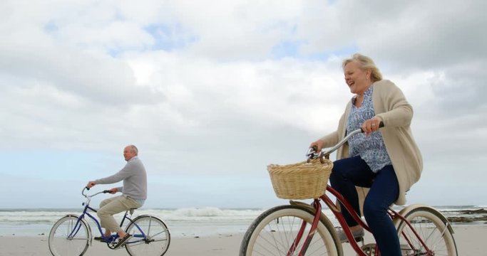 Side view of old caucasian senior couple riding bicycle at beach 4k