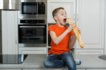 little funny boy eating a bun in the kitchen. cute baby eating baguette. Portrait of cute baby with bread in her hands. boy eat lunch in the kitchen