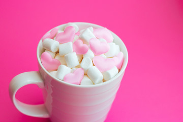Mug with marshmallows in the shape of heart on pink background