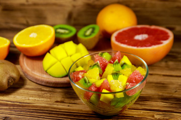 Tasty fruit salad in glass bowl and fresh fruits on the wooden table