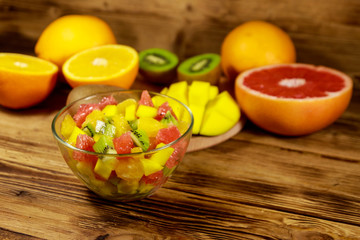 Tasty fruit salad in glass bowl and fresh fruits on the wooden table