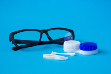 Glasses and container with contact lenses on a blue background. The concept of taking care of vision.