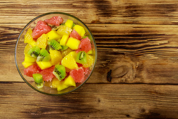 Tasty fruit salad in glass bowl on the wooden table