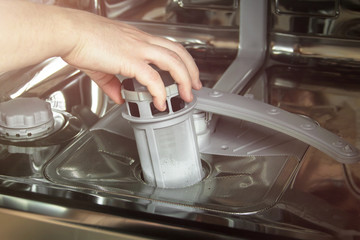 man cleans the filter in the dishwasher. Maintenance of home appliances.