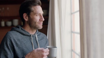 young man opening curtains looking out window enjoying fresh new day feeling rested drinking coffee at home