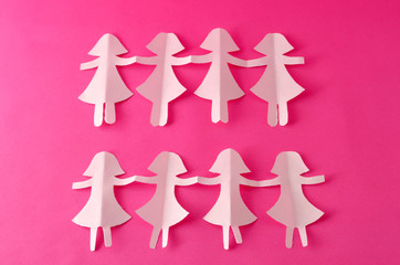 White paper doll chain on pink background. Decoration for International Women's Day