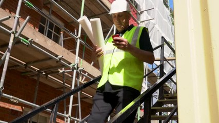 Male builder foreman, worker or architect working on construction building site holding plans walking down stairs and talking on cell phone