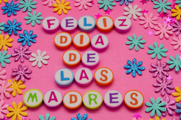 Feliz día de las madres made from colorful letters and little colorful flowers against pink background