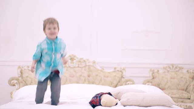 Happy little boy jumping on bed in bedroom. cute little child or toddler jumping happily at home. Curly baby boy on bed jumps before going to bed. Child is happy and fun in parents bedroom.