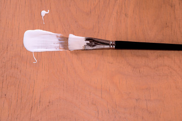 Overhead shot of brush for drawing, bristle with white acrylic paint on a light wooden Board. Art concept