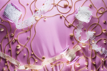 Pink reel with white lace ribbon. Pearls lie on a pink background. Golden beads scattered around...
