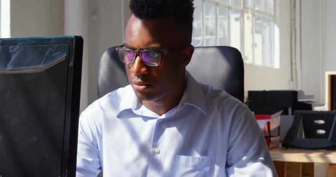 Front view of young black businessman working on desktop pc in a modern office 4k