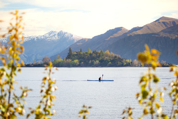 New Zealand wilderness landscape with person in distance kayaking on alpine lake in Wanaka, NZ. Outdoor adventure sports. Exploring nature and environment. People enjoying nature concept.