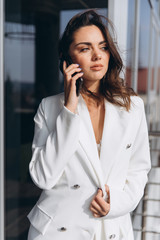 Pretty stylish business woman stands on the balcony near modern office and talking on the smartphone.