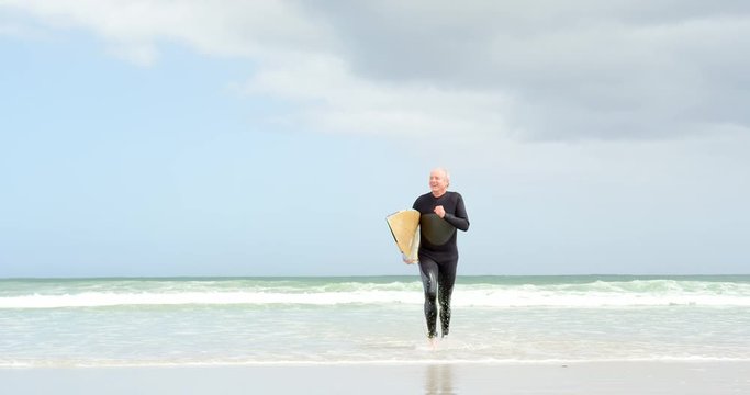 Front view of old caucasian senior man running with surfboard at beach 4k