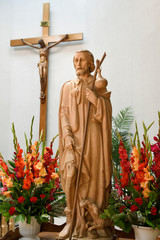 Carved wood statue of Saint Roch with plague bubo on thigh and dog with bread that saved him in...