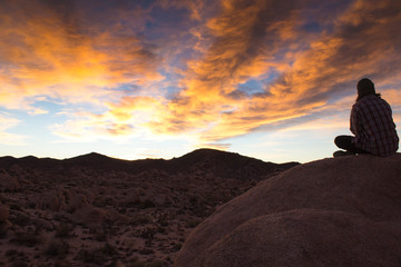 Fototapeta na wymiar A woman watches a colorful sunrise over a rocky mountain range