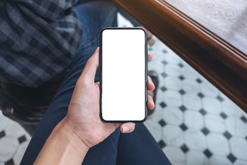 Top view mockup image of a man's hand holding white mobile phone with blank desktop screen on thigh in cafe