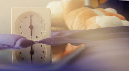 Alarm clock (6 o' clock in the morning) on the bed at home. Morning time background concept, soft focusing and vintage color style.