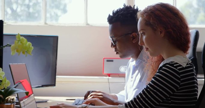 Side view of young mixed-race business team working on laptop and desktop pc in a modern office 4k