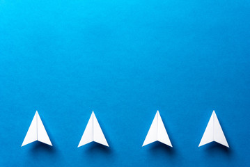 Line of four white paper airplanes, leadership, teamwork, motivation concept on blue background