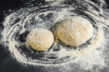 Pizza dough or baking on a dark black background of wood. Baking bread, pizza, pasta. Top view, horizontal photo