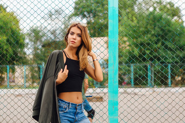 Fashion portrait of trendy young woman wearing sunglasses, jeans with halls and bomber jacket in...
