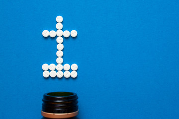 white pills in the shape of a grave cross are scattered on a blue background next to a dark bottle. Depression, harm of drugs concepts. Top view with copyspace