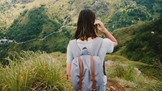 Back view young tourist woman with backpack steps down extremely steep mountain path, epic view in Sri Lanka slow motion