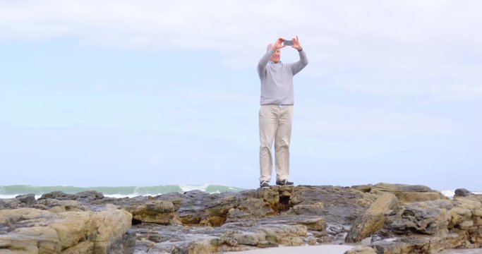 Front view of old caucasian senior man clicking photo with mobile phone at beach 4k