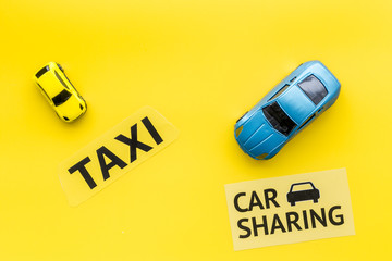 Carsharing vs taxi concept. Comparing carsharing system and taxi. Ship trip concept. Toy cars and text signs on yellow background top view copy space