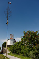 Maypole with Slovenian flag and wreath at Saint Vitus Catholic church and cherry trees in Vedrijan Brda Slovenia