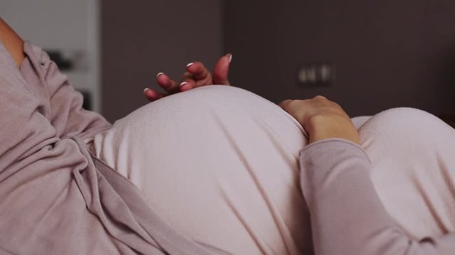 Pregnant woman feels her future baby pushing on a bed at home - Front View