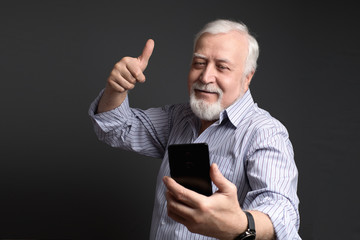 good-natured smiling man makes selfie on a mobile smart phone on a gray background