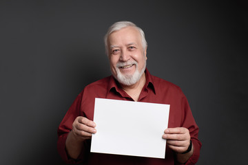 good-natured smiling man on a gray background holding a sheet of white paper for the inscription