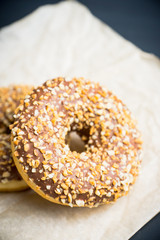 Donut with chocolate glaze and crashed nuts on the rustic background. Selective focus.