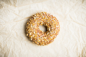Donut with chocolate glaze and crashed nuts on the rustic background. Selective focus.